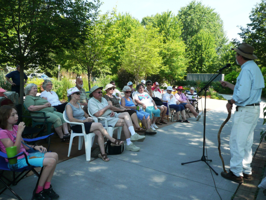 man stands in front of an audience in an outdoor garden